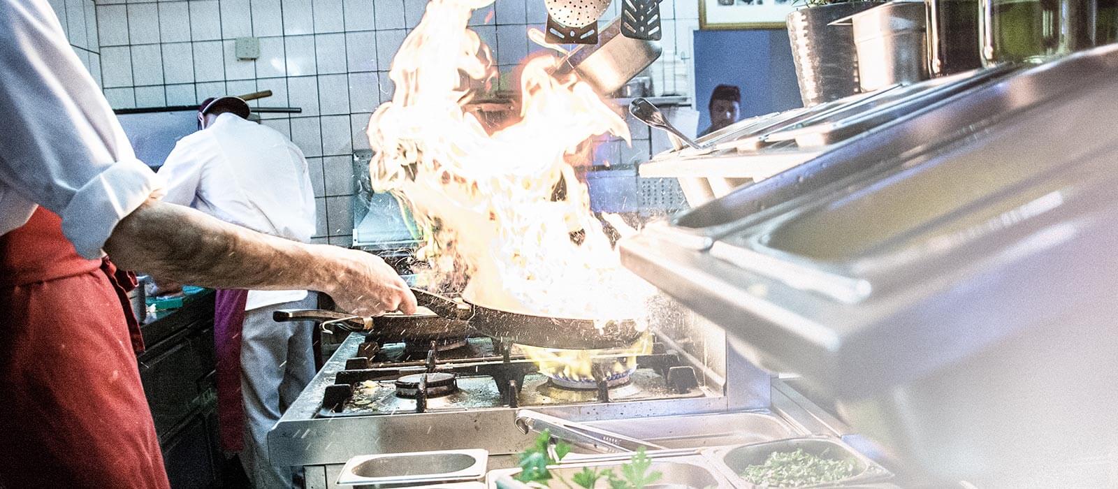 Koch flambiert mit hohen Flammen in der Küche